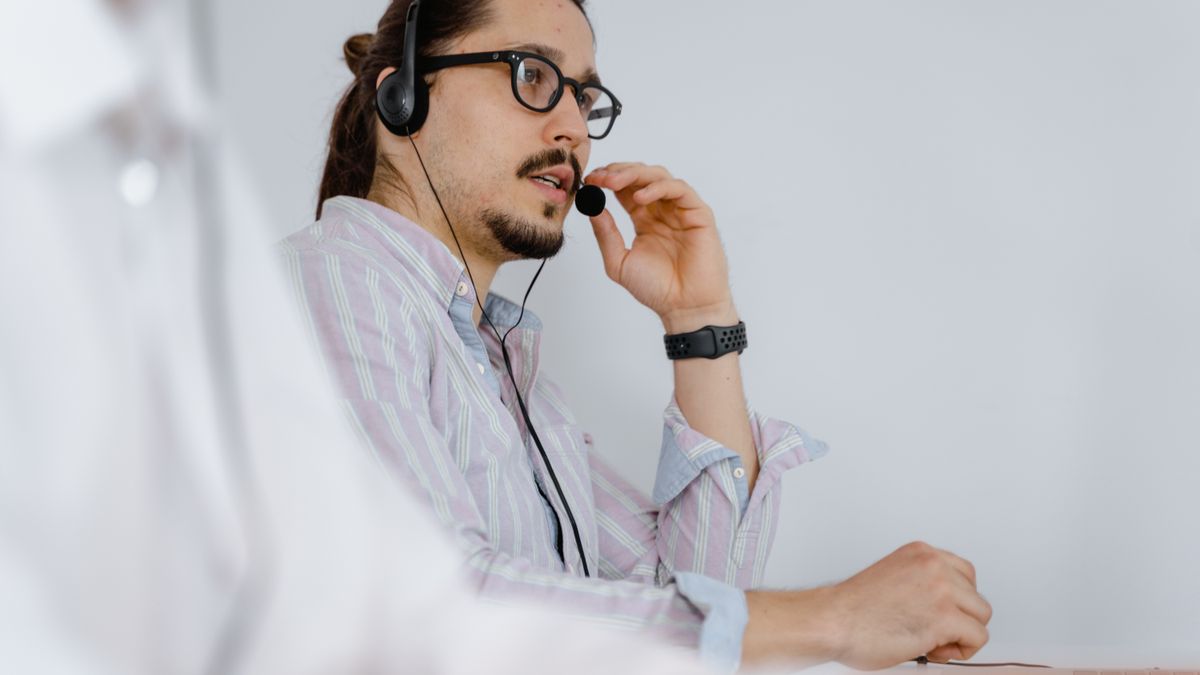 Atendente de suporte conversando com consumidor ao telefone em mesa de trabalho