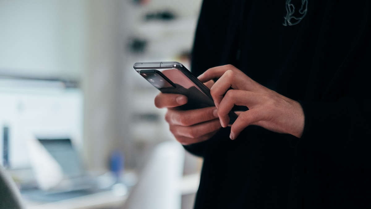 Mãos segurando celular com mensagens ofensivas e assédio virtual